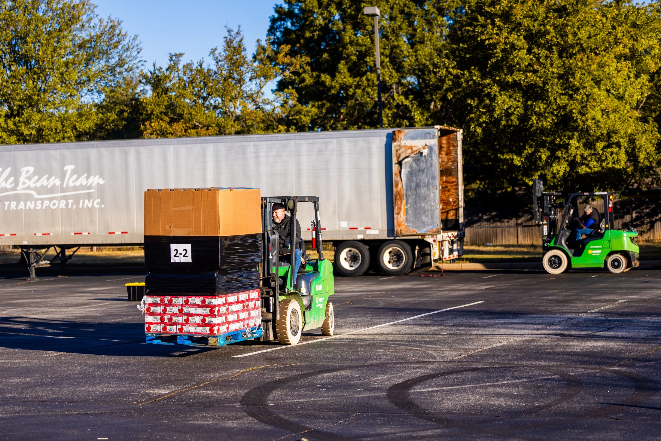 Forklift operators moving palletized cargo beside a trailer